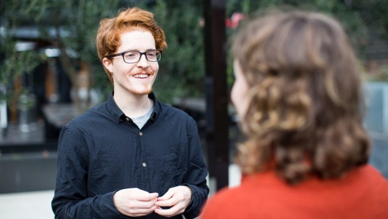 Man with orange hair talking to woman in orange jumper