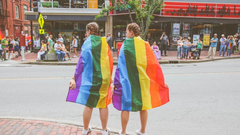 Two people wearing rainbow flag capes
