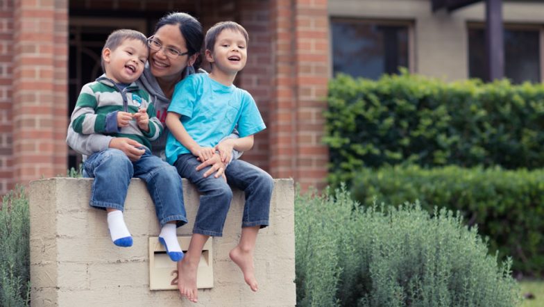 Mother and two children sitting happily outside their house