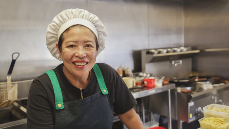 Woman of colour smiling wearing a chef's hat in a commercial kitchen